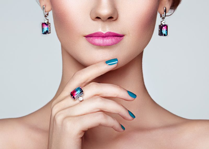 Imagen parcial de una mujer con conjunto de joyería de pendientes y anillo.